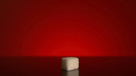 Single cube of sugar isolated on red background. Close up of a white sugar cube standing in the shadow with bright light shining then.の写真素材