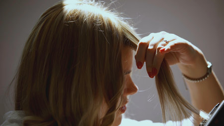 The girl winds curls on a curling iron. The girl has blond hair that she curls. straightener curl hairの写真素材