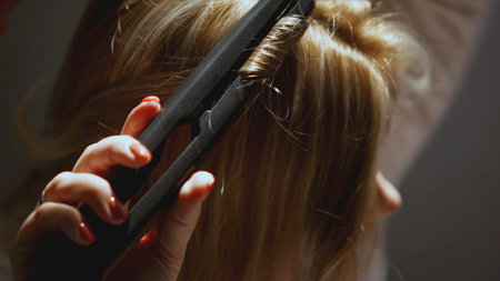 The girl winds curls on a curling iron. The girl has blond hair that she curls.の写真素材