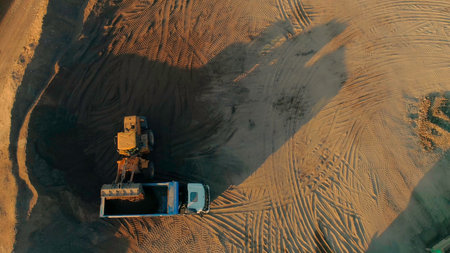 Excavator removing sand into dump truck. Scene. Top view of excavator loading sand into truck. Construction and grinding works with sandの写真素材