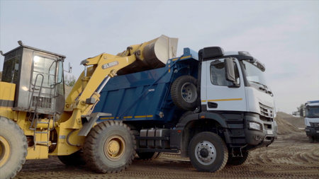 Side view of a mining truck with its bucket loaded with sand. Scene. Heavy industry and machinery...