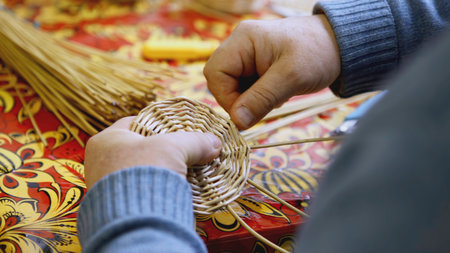 Hands weaving the bottom of a straw basket. A man weaves a round part of straw and twigs with his hands. Crafts are learned at the festivalの写真素材