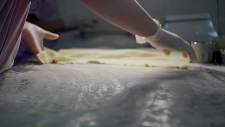 Close up of a hand in glove putting flour on a table and a sheet of dough. Clip. Process of...
