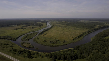 Aerial view of a bending river flowing and crossing wide green field. Stock footage. Summer rural...