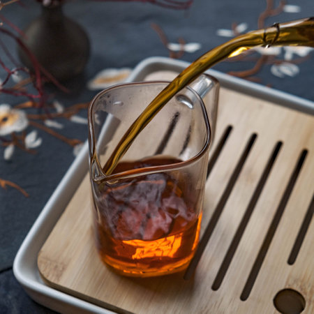 Pouring a delicious cup of Tea into a clear Glass Beaker filled with refreshing Iceの写真素材