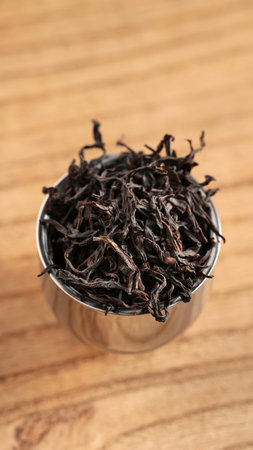 A Collection of Dried Tea Leaves Resting in a Metal Scoop on a Smooth Wooden Surface