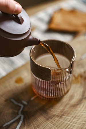 Pouring tea meticulously from a charming teapot into a delicate glass cup brings joyの写真素材