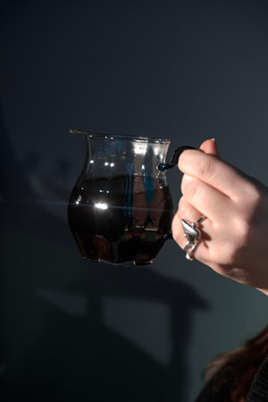 An Elegant Hand Gracefully Holding a Beautiful Glass Jug That is Filled with Dark, Rich Liquidの写真素材