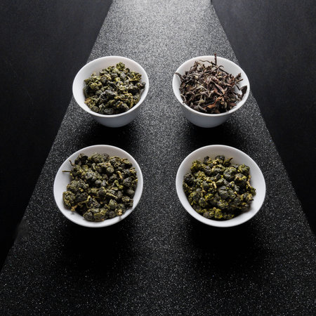 A Beautiful Selection of Assorted Loose Teas Artfully Arranged in White Bowls on a Dark Surface