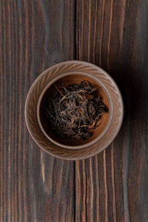 A Bowl Filled with Dried Black Tea Leaves Placed on a Rustic Wooden Table Surface