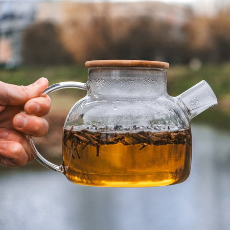 A Beautiful Glass Teapot Filled with Herbal Tea Set Against a Stunning Scenic Backgroundの写真素材
