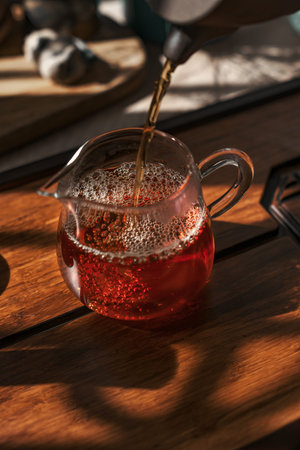 Carefully pouring aromatic tea into a beautiful glass jug that rests on a lovely wooden table