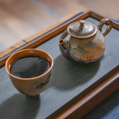 A beautiful and traditional tea pot along with a cup is elegantly placed on a wooden tray