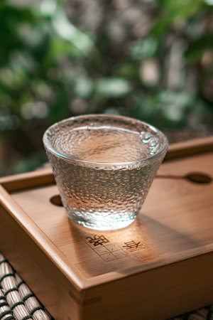 An elegant glass cup filled with refreshing water resting beautifully on a wooden trayの写真素材