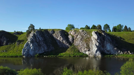 A picturesque scenic rock formation located near a tranquil river beneath a clear blue sky. Stock...