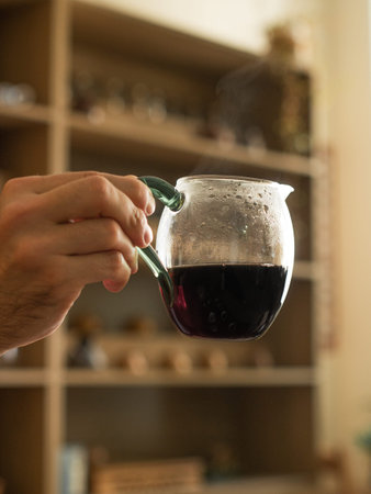 A hand is gently holding a glass jug filled with a rich, dark liquid that looks inviting