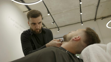 Professional barber carefully trimming clients beard. Clipの写真素材