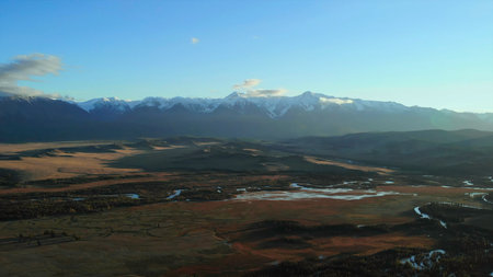 Snowy mountain range dominating autumnal valley under blue sky.の写真素材