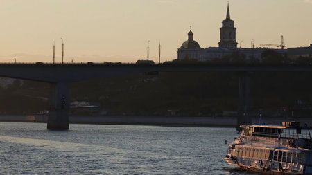 Passenger ferry navigating river at sunset near bridge and church. Clipの写真素材