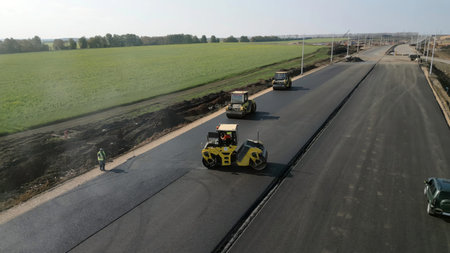Road rollers compacting fresh asphalt on a new road. Clip