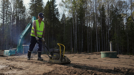 Construction worker compacting soil with vibratory plate compactor. Clip