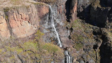 majestic cascade over basalt cliffs, spectacular waterfall plunging down layered volcanic rock...