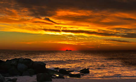 Beautiful sunset on an ocean coast, a ship silhouette in beams of the coming sunの写真素材