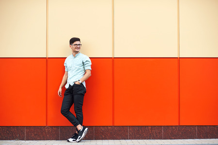 Full-length shot of smiley man standing against huge orange wall looking on the leftの写真素材
