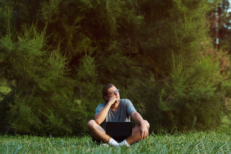 A young handsome male with notebook outside. Serious confident boy thinking about future while sitting on grass in public park.の写真素材
