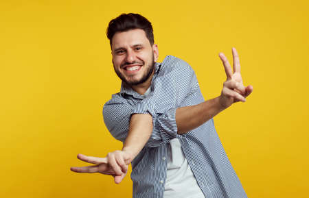Excited handsome male dressed in stylish shirt and showing peace gesture with crossed hands isolated over orange backgroundの写真素材