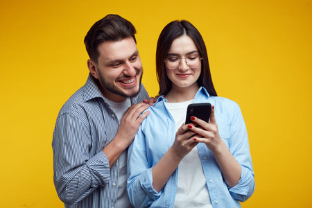 Couple embrace each other, look joyfully at mobile phone