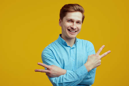 Young man dressed in blue shirt showing peace gesture with crossed handsの写真素材