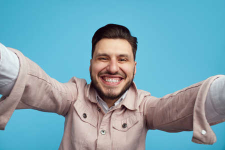 Man in pink jacket laughing at camera taking selfie on blue backgroundの写真素材