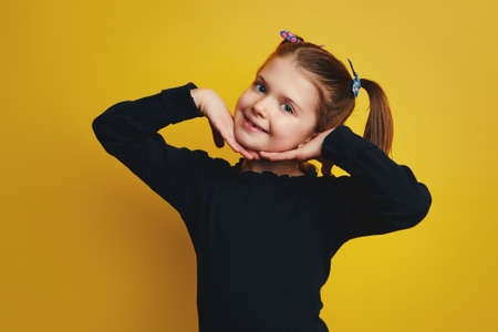 Girl holding hands on cheeks smiling at camera isolated over yellow wallの写真素材