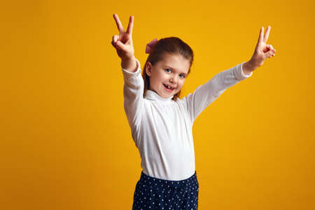 Girl showing peace gesture with both raised hands against yellow backgroundの写真素材