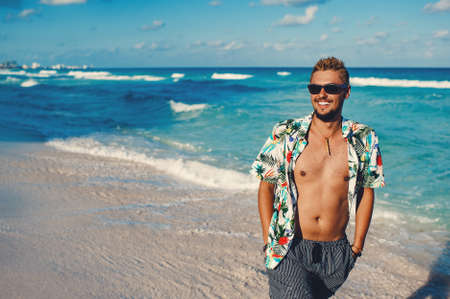 Attractive young man wearing hawaiian shirt at the sea or the ocean background. Travel vacation holiday. Man walking at the sea, enjoy tropical seasonの写真素材