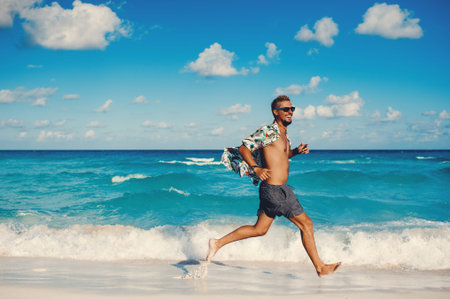 Young handsome tourist man running cheerful on the island beach while smiling against blue sea and...