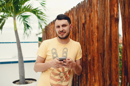 Young handsome man using mobile phone, stands above of a wooden fence or wall