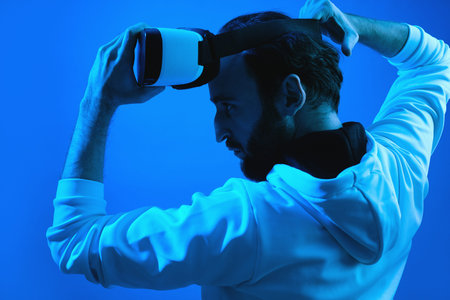 Blue neon photo of serious bearded man gamer ready to put the VR goggles on and dive into virtual...