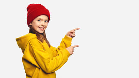 Hipster girl kid, points with both forefinger on copy space for your advertising, has excited surprised happy expression, isolated on white backgroundの写真素材