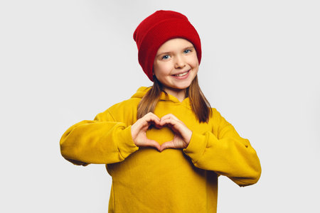 Horizontal shot of happy girl shows heart gesture, express love, say be my valentine, keep hands on...
