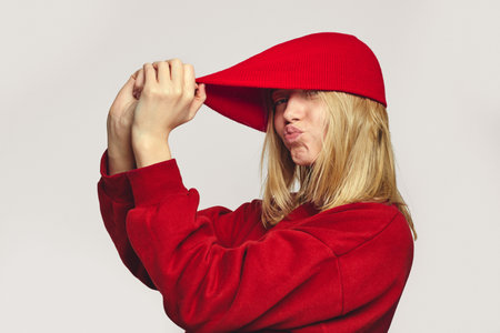 Stylish hipster girl in red outfit, pull hat outside, blow kiss at camera, isolated over white backgroundの写真素材