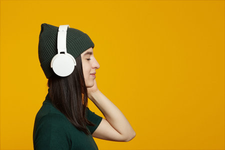 Side view of young woman wear green outfit, listen music in white headphones with closed eyes,...