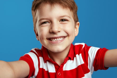 Cheerful cute preschool boy in red striped polo shirt looking at camera in amazement and taking...