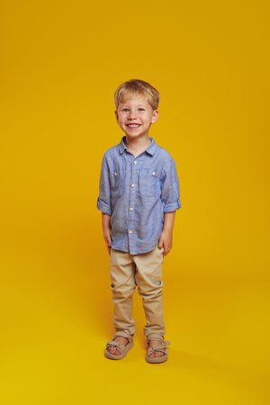 Vertical photo of full body positive kid in trendy blue shirt and beige pants smiling for camera,...