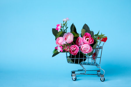 A miniature shopping cart filled with vibrant pink roses against a pastel blue background, representing beauty, shopping, and floral arrangements. Ideal for spring themes and creative concepts.の写真素材