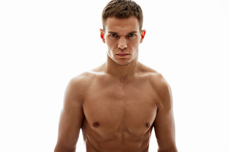 A focused young man with a muscular build, shirtless against a seamless white background. The lighting accentuates his features and defines his physique, conveying strength, focus, and determination.の写真素材