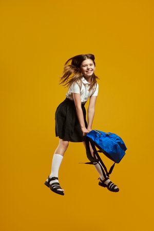 Happy child jumping energetically while holding a bright blue backpack, expressing excitement and...