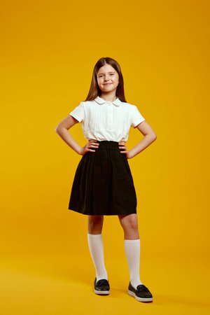 A cheerful child standing confidently with hands on hips in a classic school uniform against a...