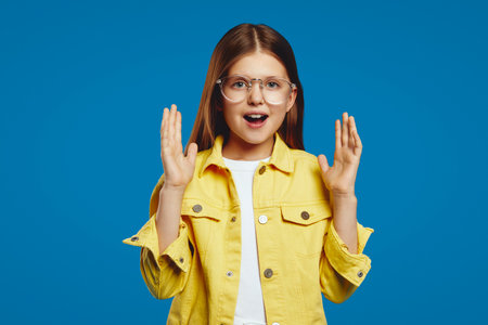 Delightful youngster wearing glasses joyfully expresses surprise in a vibrant yellow jacket, conveying positivity and wonder.の写真素材